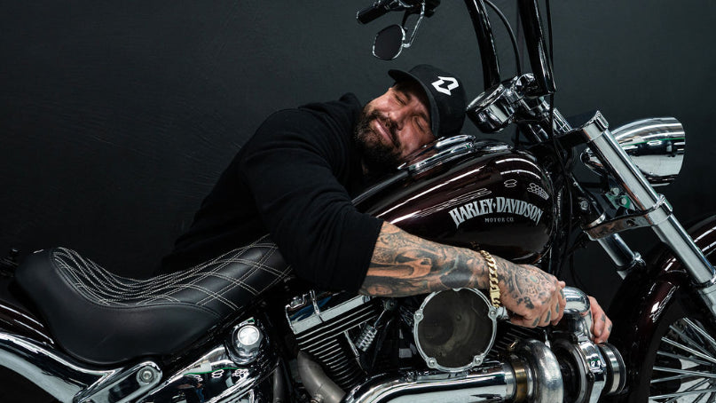 Person with tattoos sitting on a Harley Davidson motorcycle against a dark background