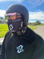 Person wearing a helmet and face mask with visible branding, outdoors on a road.