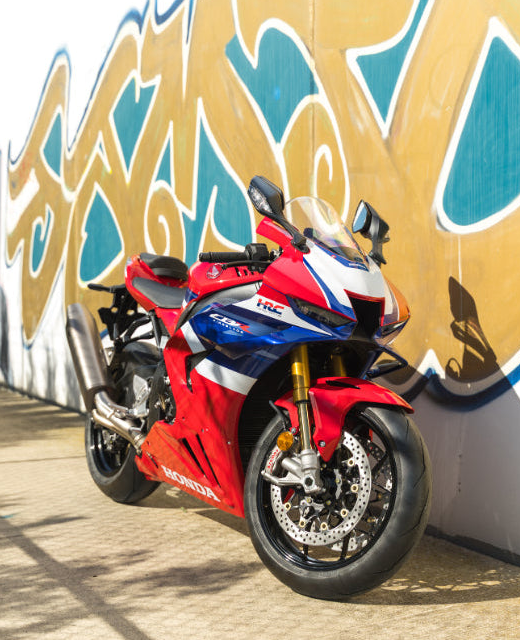 A red, white, and blue Honda CBR1000RR sport motorcycle parked outdoors against a graffiti-covered wall.